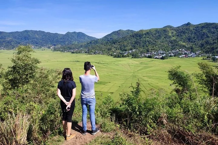 Two tourists overlooking the expansive, spider-web patterned rice fields from a viewpoint.