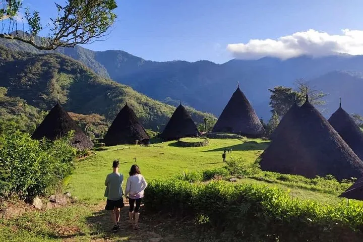 Turisti che camminano verso le case coniche del villaggio tradizionale di Wae Rebo sotto la luce del sole.